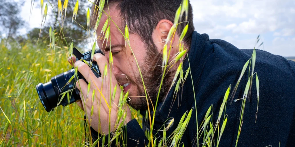 צלם בצילום טבע בשטח פתוח בין עשבים ירוקים, תקריב מהצד